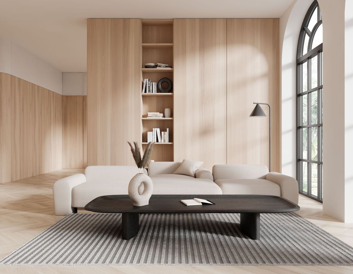 Salon minimaliste avec canapé d'angle beige, table basse noire, lambris et haute fenêtre cintrée.