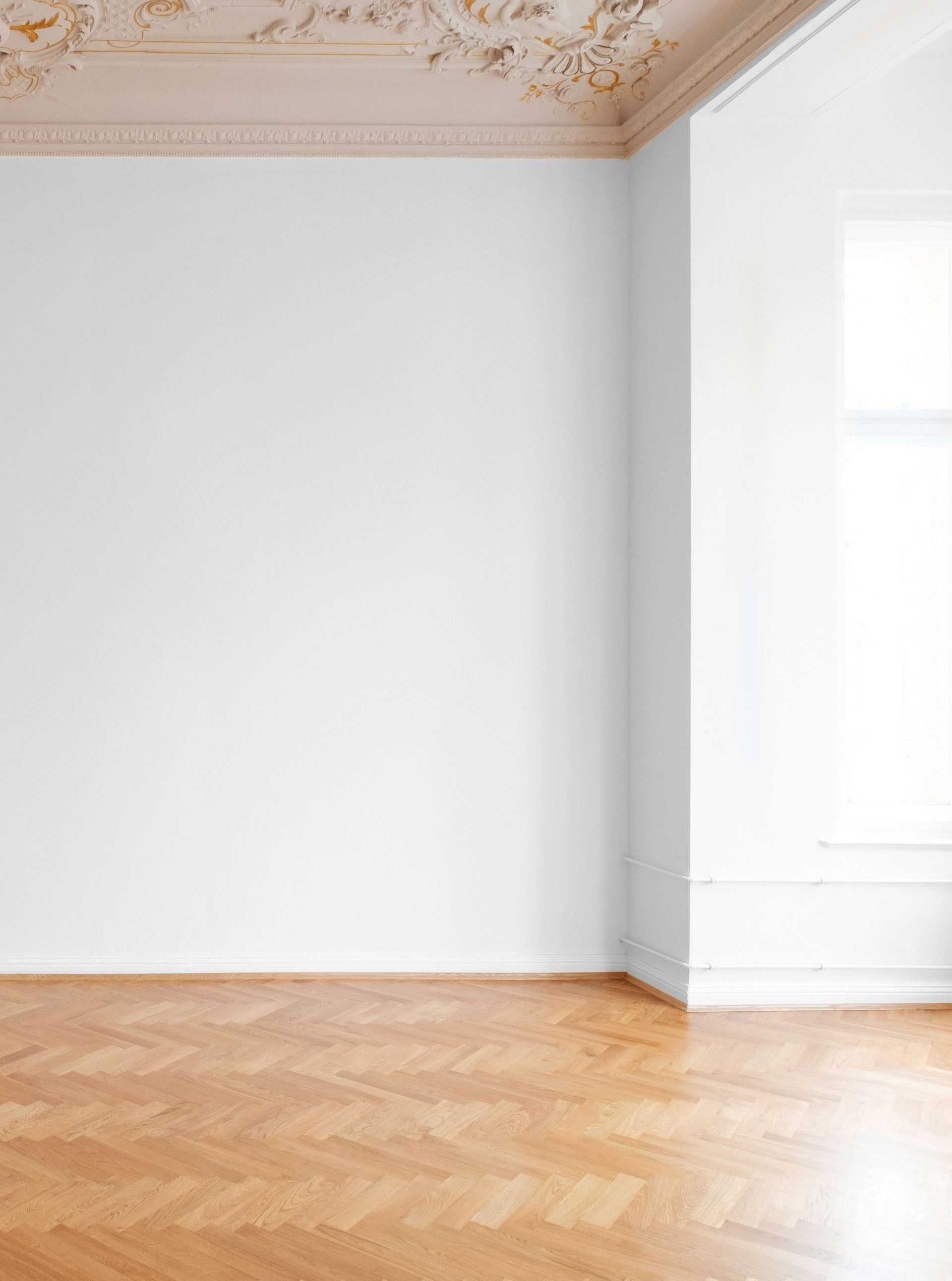Pièce blanche vide avec moulures de plafond ornementées et parquet en chevrons.