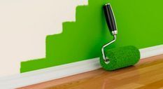 Un rodillo de pintura verde está sobre un piso de madera al lado de una pared verde.