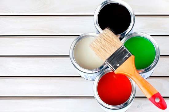 Cuatro latas de pintura y un pincel sobre una mesa de madera.