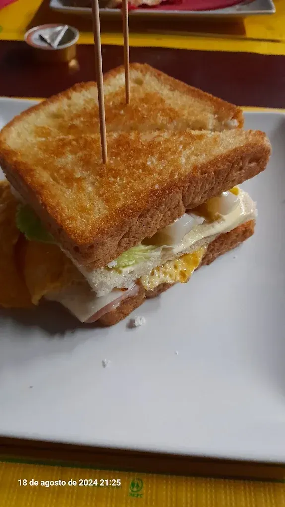 Sándwich tostado con huevo y queso fundido en un plato blanco, sujeto con un palillo.