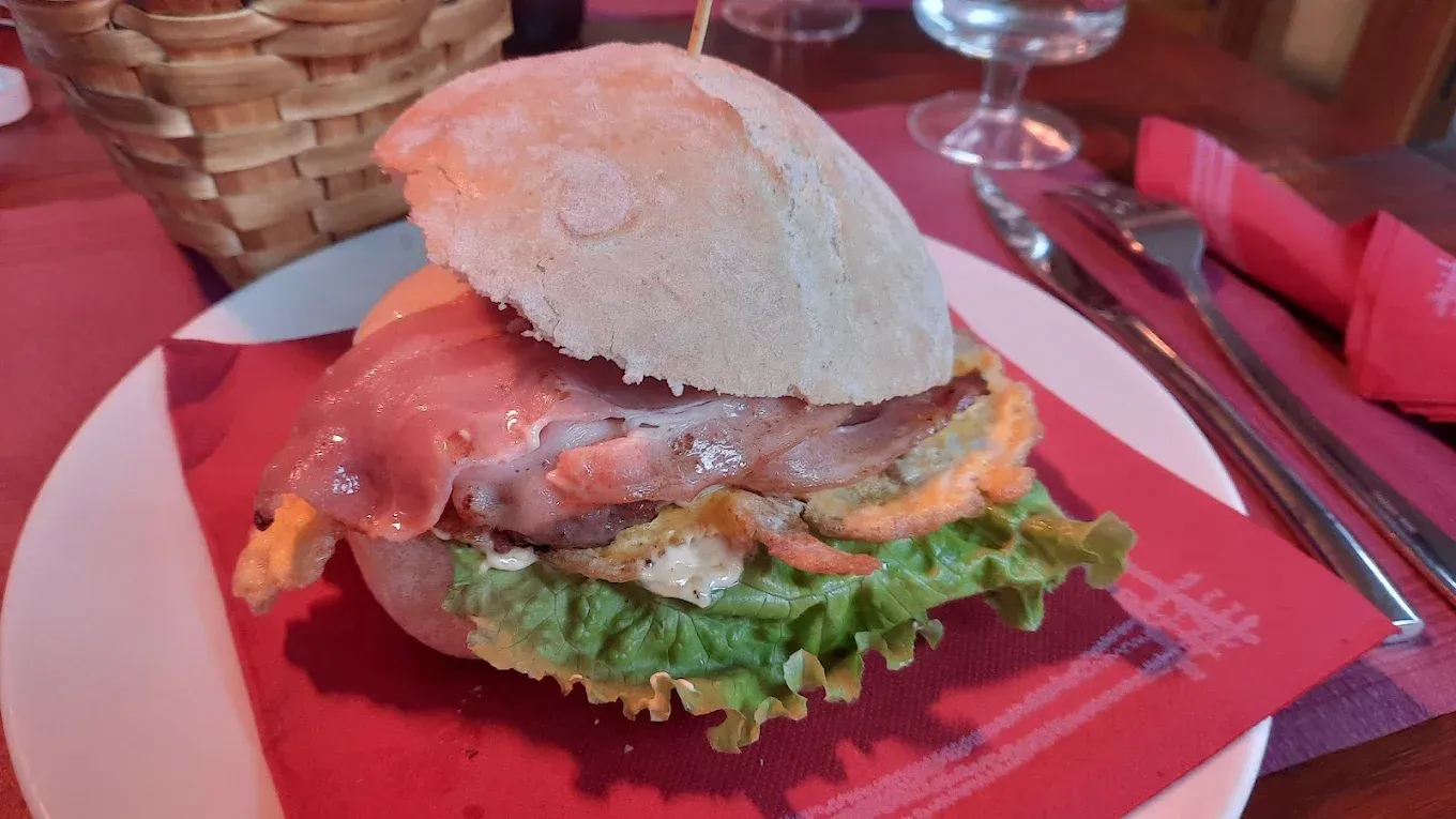 Hamburguesa con lechuga y tocino en un plato rojo en una mesa de restaurante.