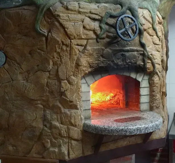 Horno de pizza de piedra con fuego incandescente en su interior y una manivela sobre la abertura.