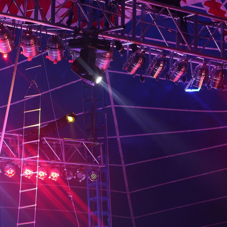 Structure de scène de concert éclairée en violet avec projecteurs suspendus et faisceaux laser.