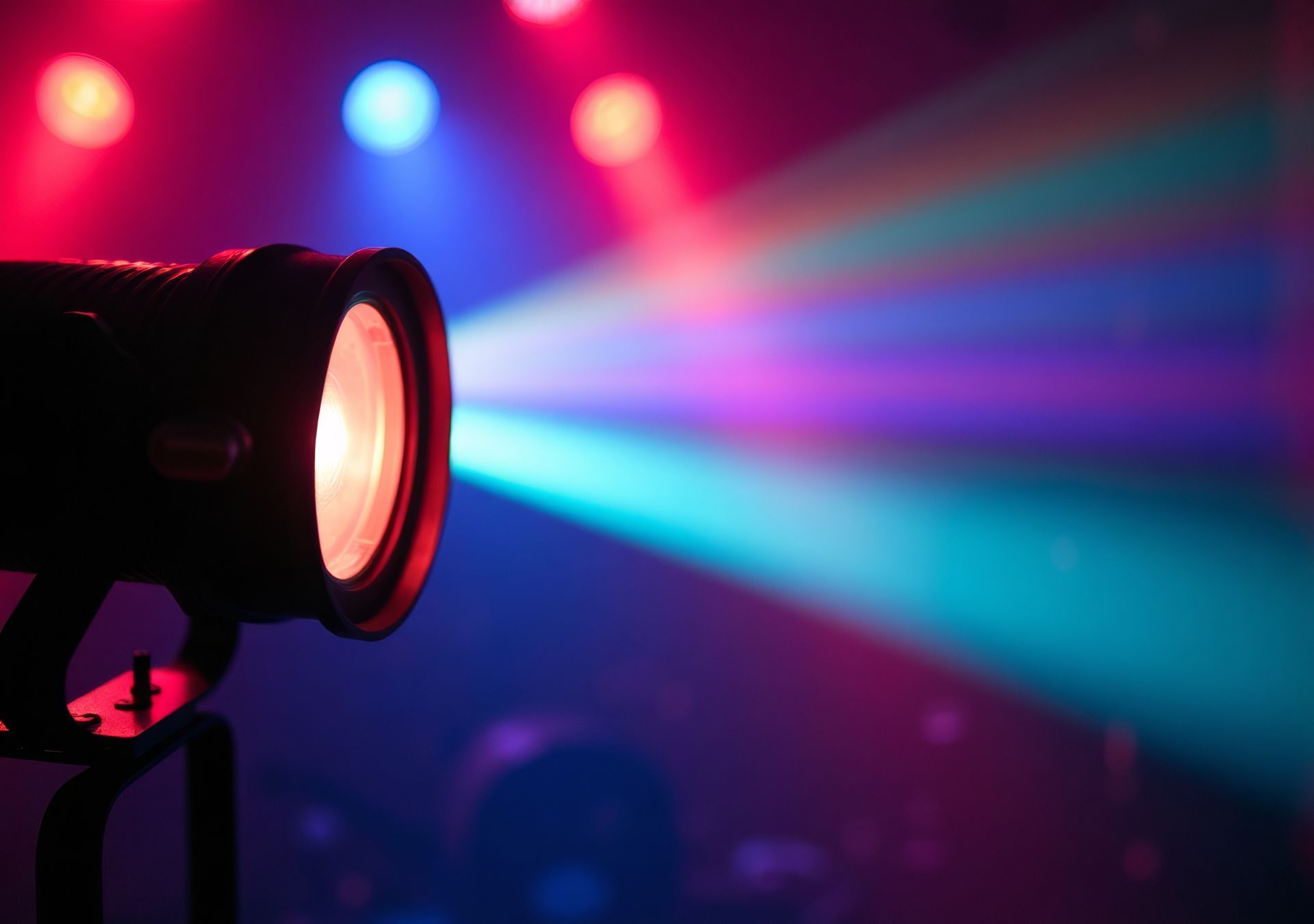 Un projecteur de scène avec des faisceaux roses et bleus illumine la scène dans l'obscurité d'une salle de concert.