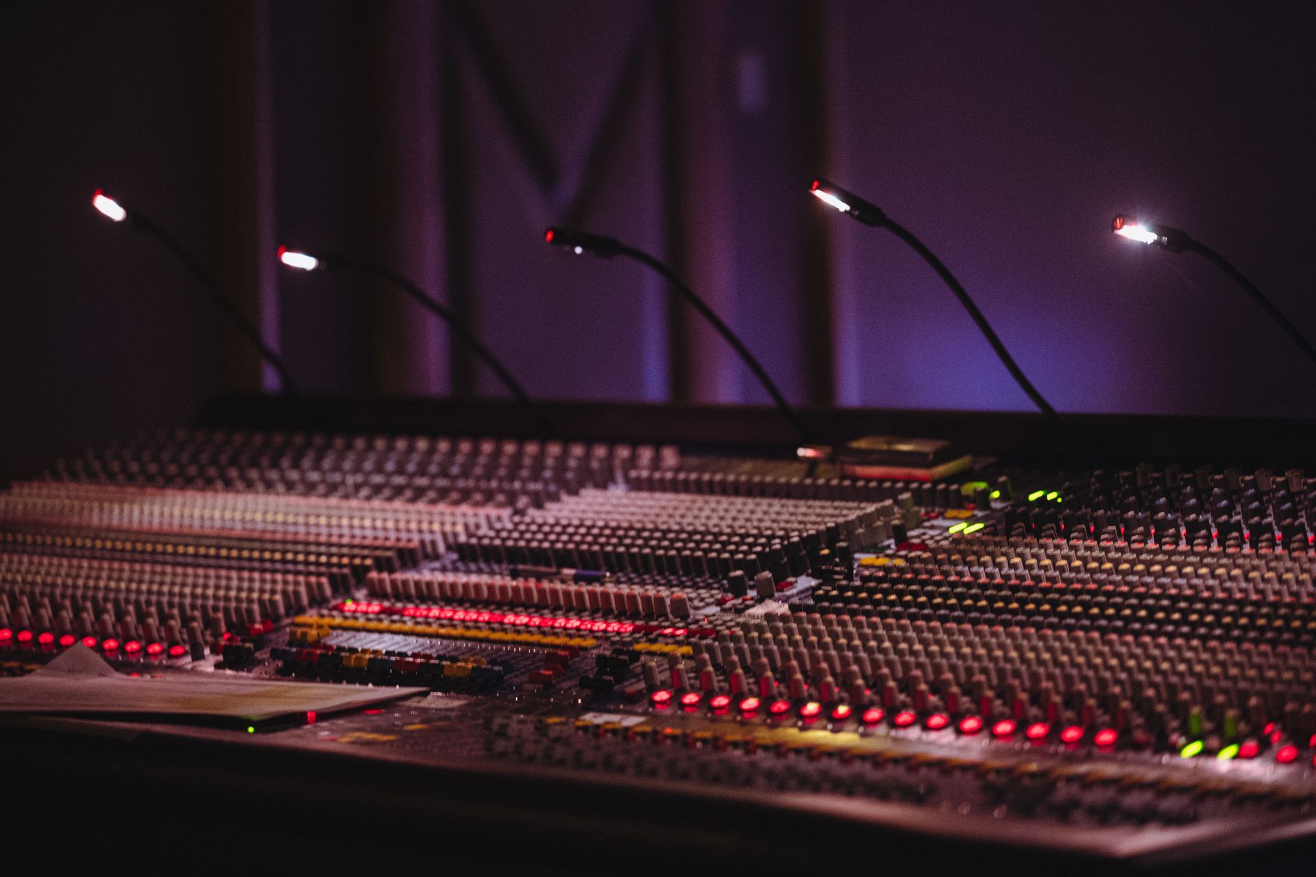 Console de mixage audio avec commandes et microphones lumineux dans un studio sombre.