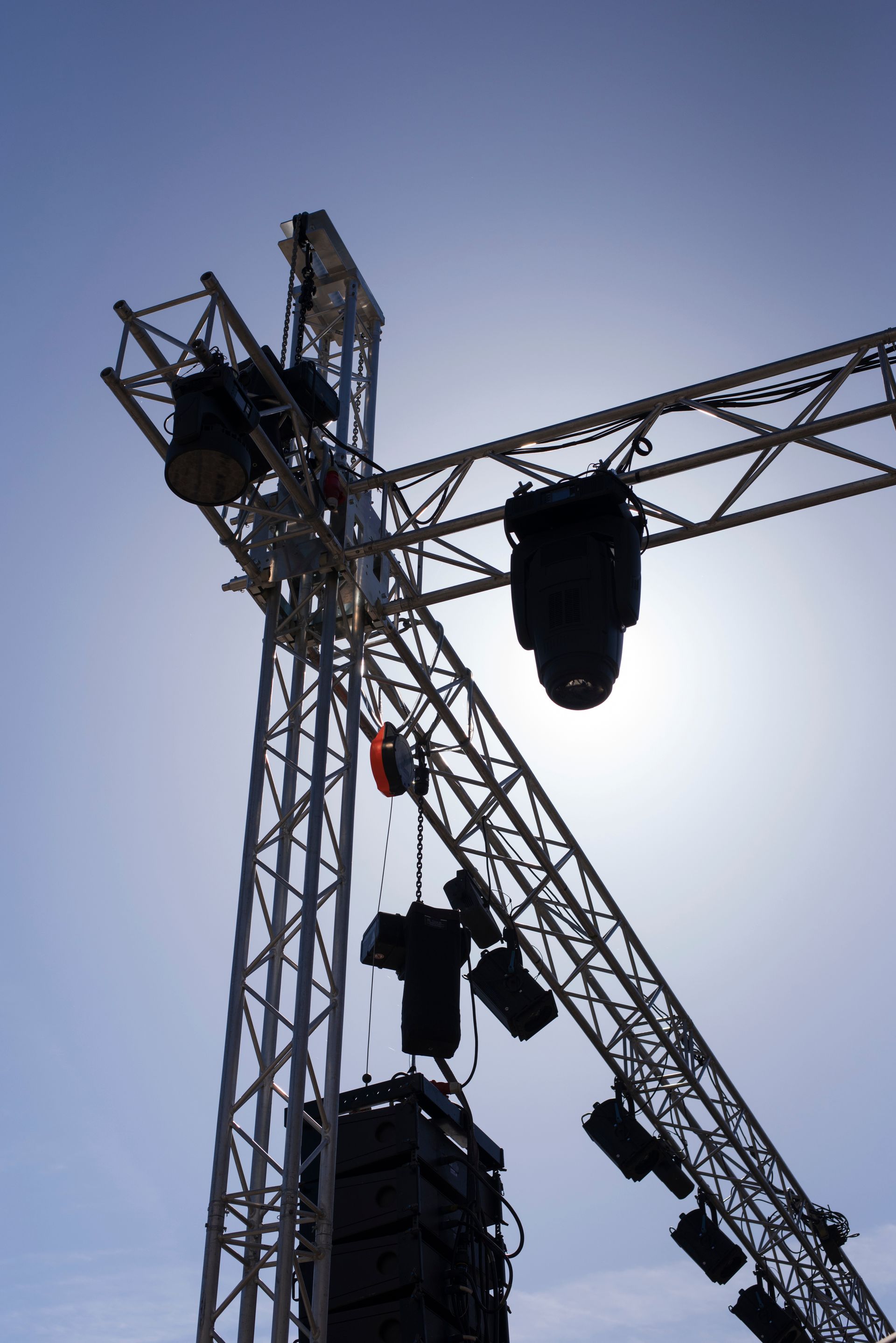 Structure d'éclairage scénique se détachant sur un ciel lumineux, avec des projecteurs suspendus à une structure métallique.