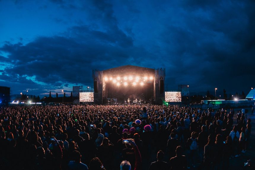 Concert en plein air bondé, la nuit, avec une scène illuminée.