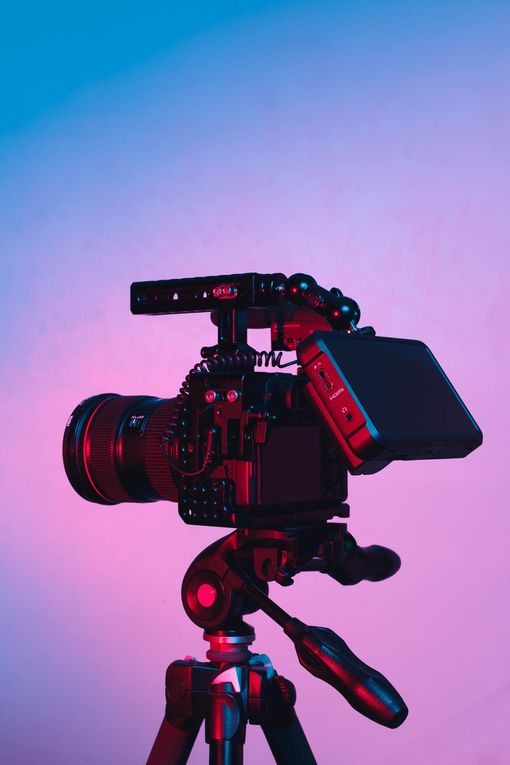 Caméra vidéo professionnelle sur trépied devant un fond dégradé bleu et rose.
