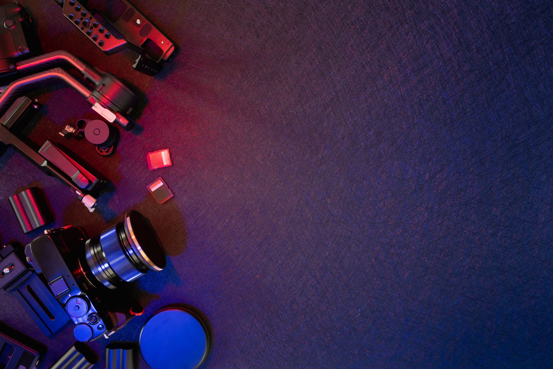 Vue de dessus d'un appareil photo, d'un objectif et d'accessoires sur une surface sombre éclairée en rouge et bleu.