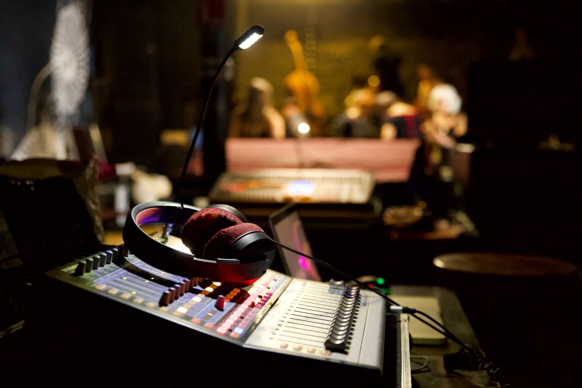 Console de mixage audio avec casque dans un studio faiblement éclairé, avec des personnes floues en arrière-plan.