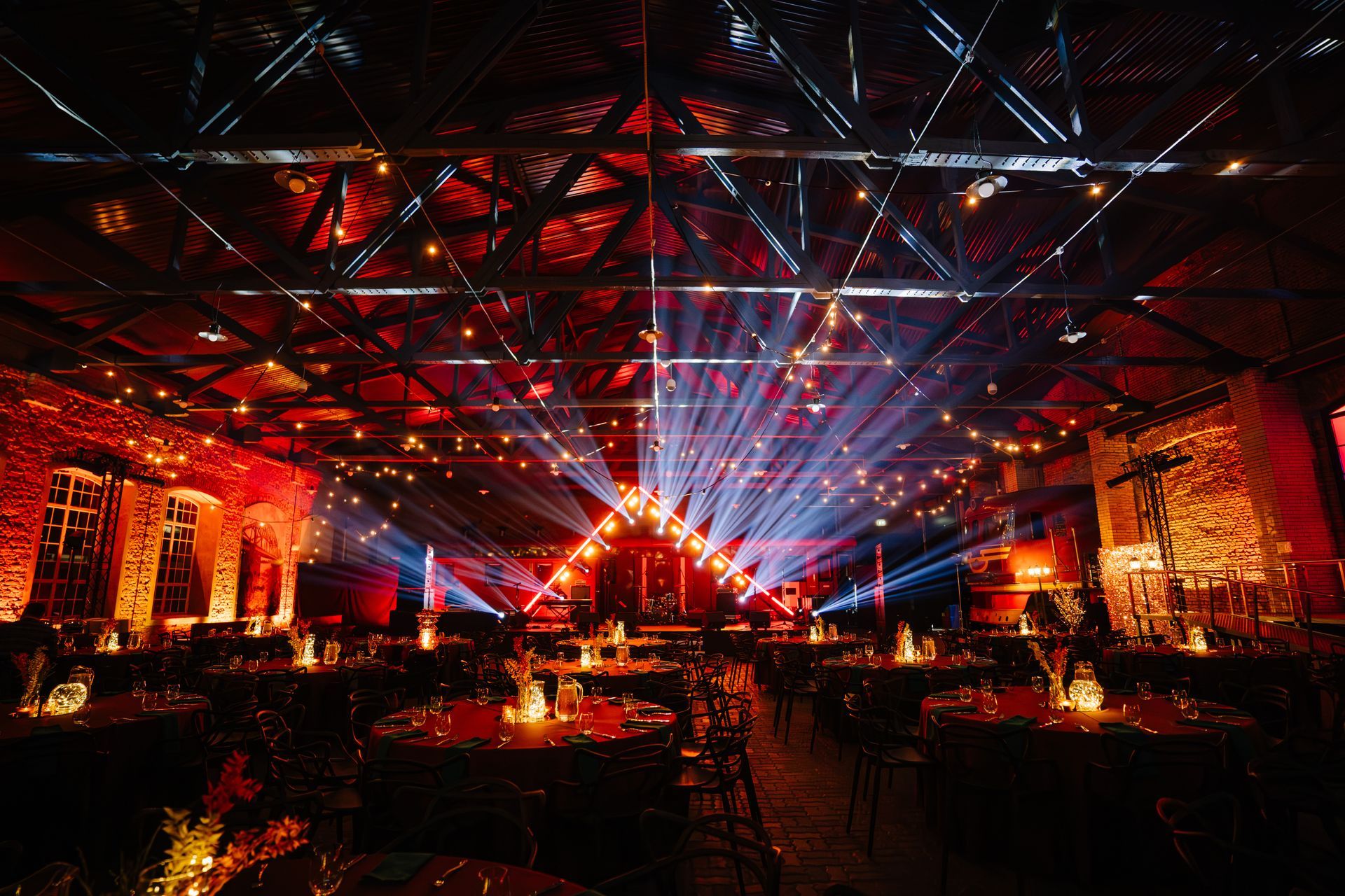 Scène de concert dans une grande salle éclairée en rouge et illuminée par des faisceaux laser bleu vif au plafond.
