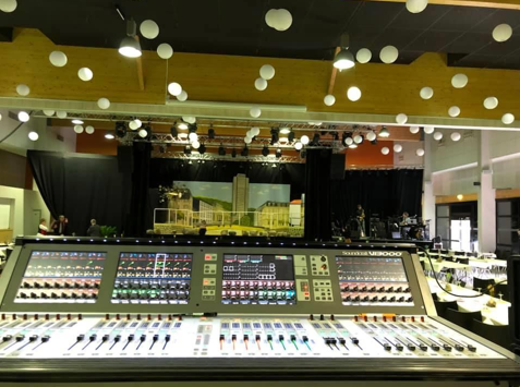 Grande console de mixage audio avec des rangées de commandes et une scène en arrière-plan.