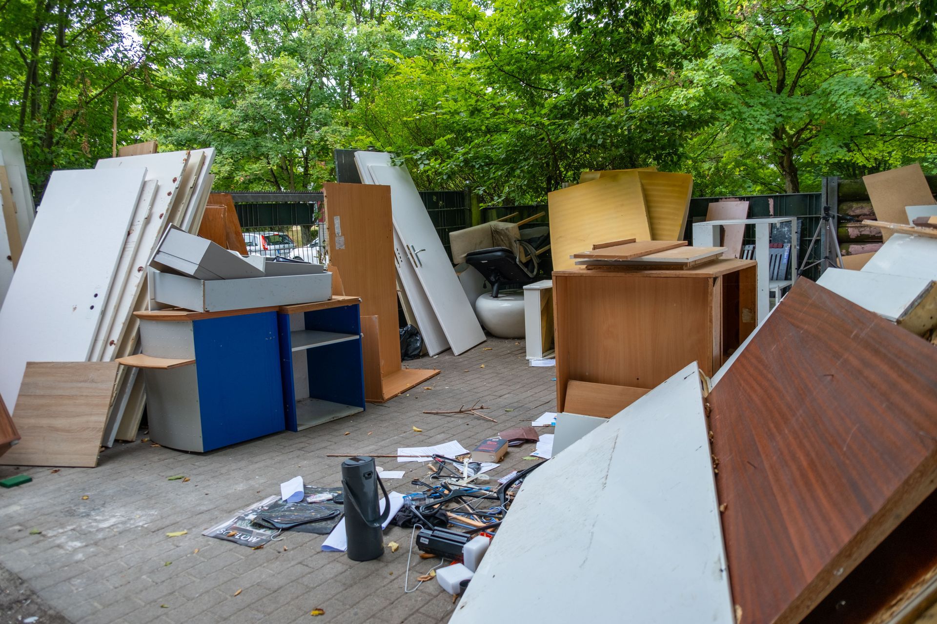 Des tas de meubles et de débris abandonnés jonchent un trottoir près d'arbres, laissant supposer un dépôt illégal.