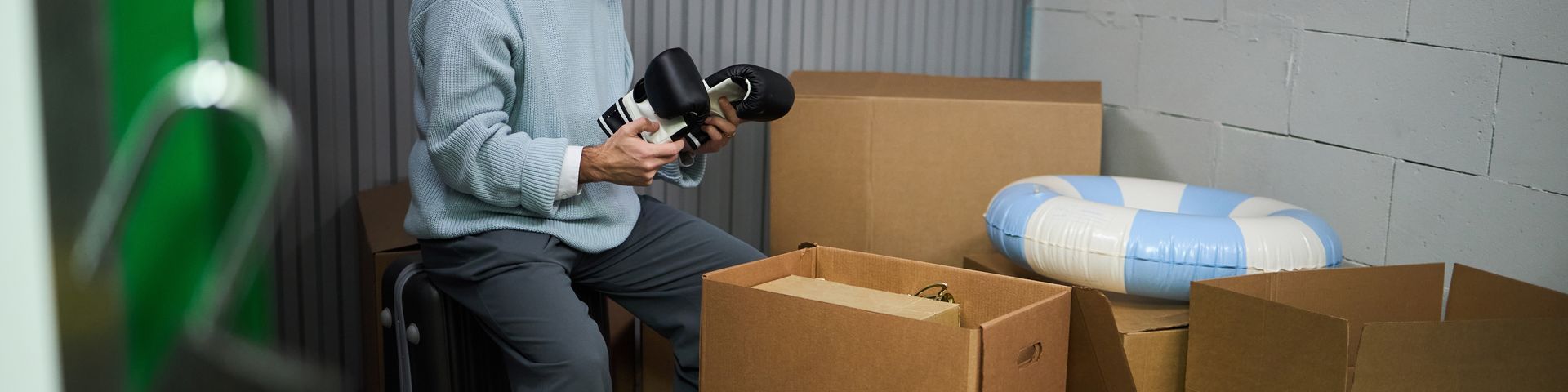 Une personne accroupie dans un entrepôt, en train d'emballer des cartons à côté de paquets emballés dans du papier bleu et blanc.