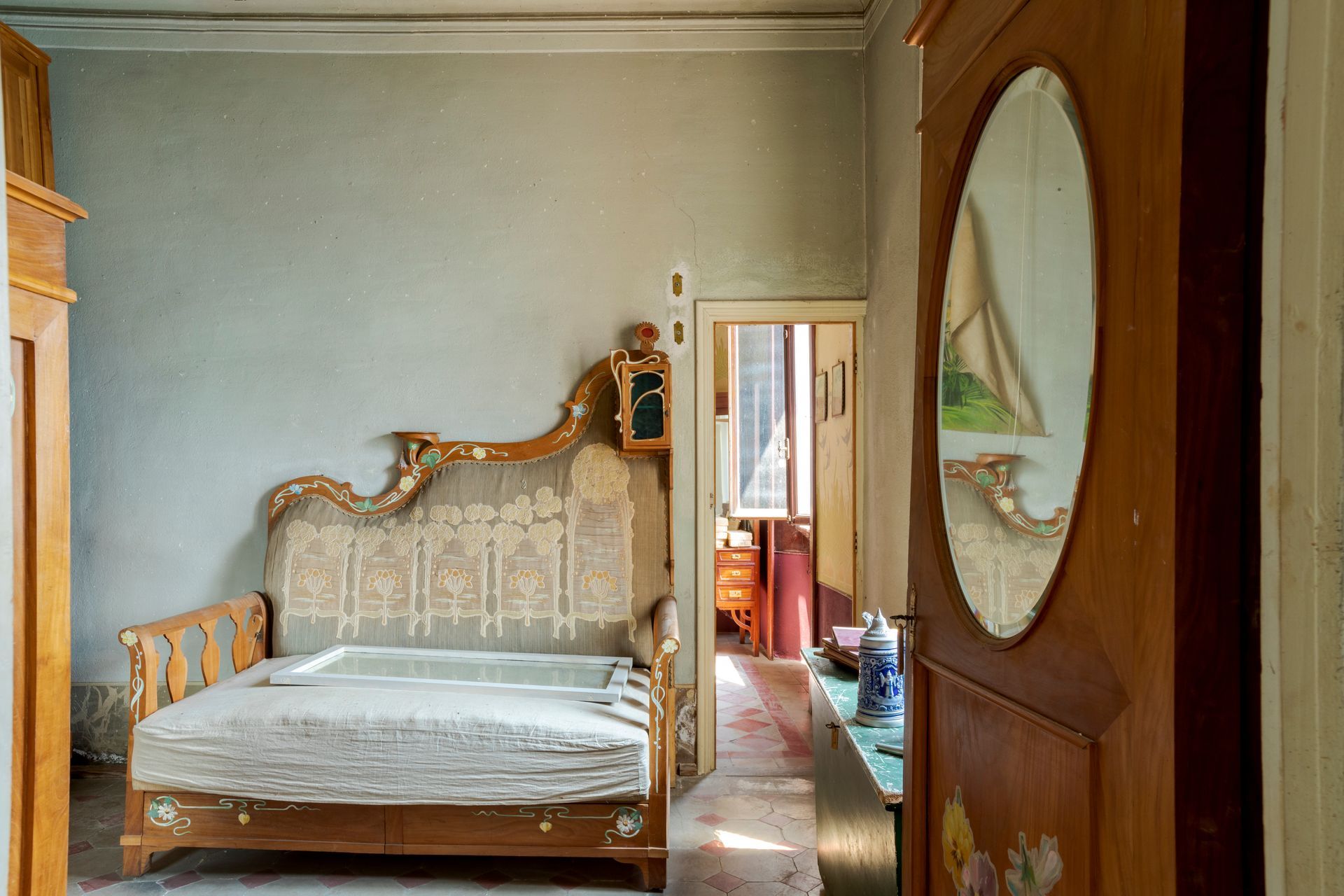 Chambre vintage avec lit en bois orné, murs bleu pâle et porte ouverte sur un couloir