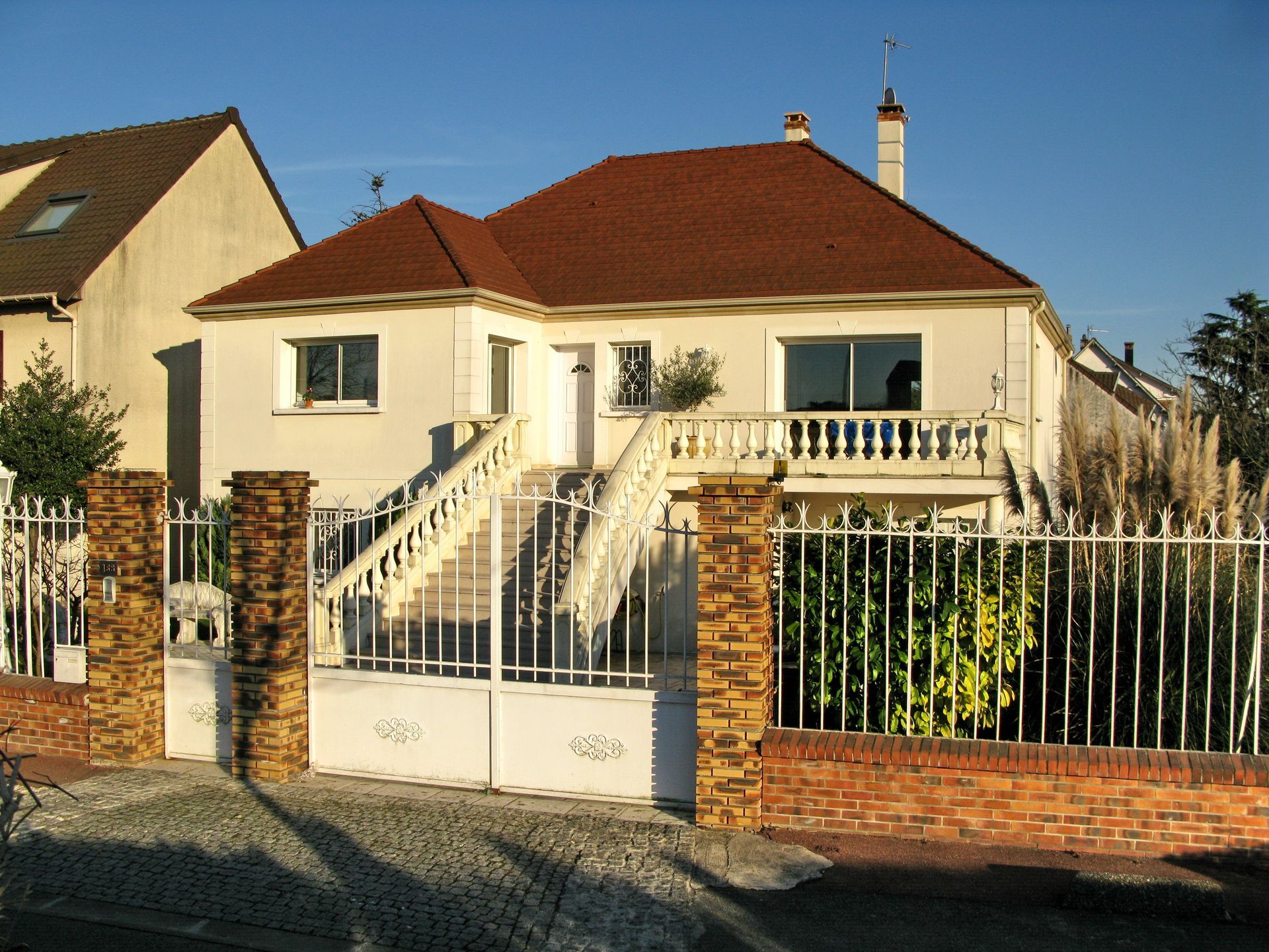 Un pavillon au toit rouge derrière une grande grille blanche.