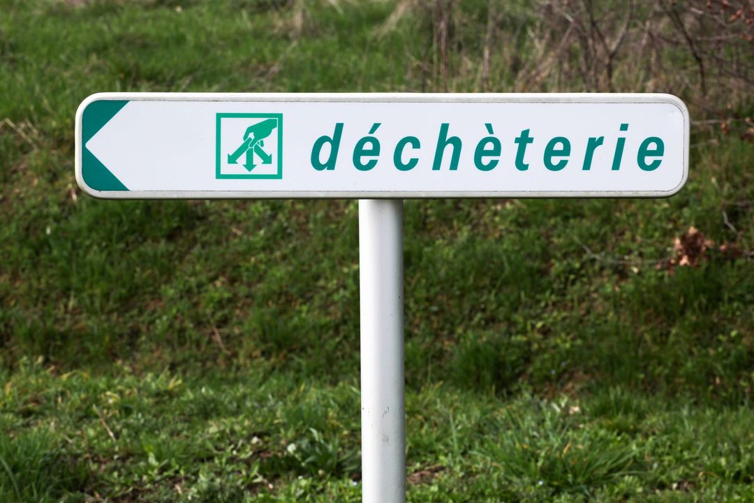 Panneau routier indiquant « déchèterie » avec un symbole de recyclage vert sur un poteau blanc.