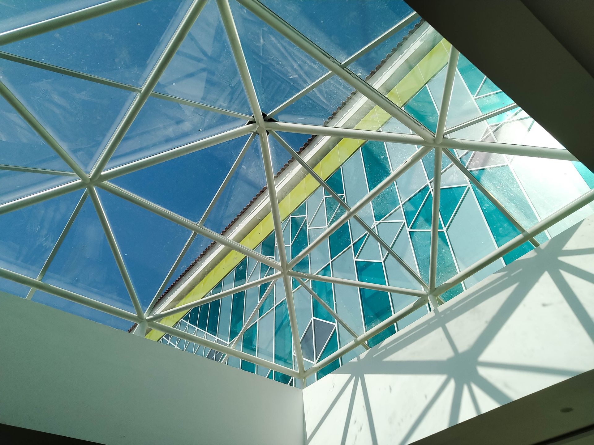 Plafond vitré avec vue sur le ciel bleu et poutres métalliques géométriques projetant des ombres