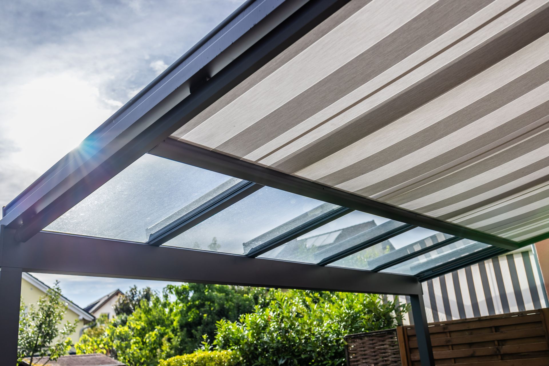 Patio couvert avec un toit rayé transparent et un ensoleillement sur un jardin verdoyant