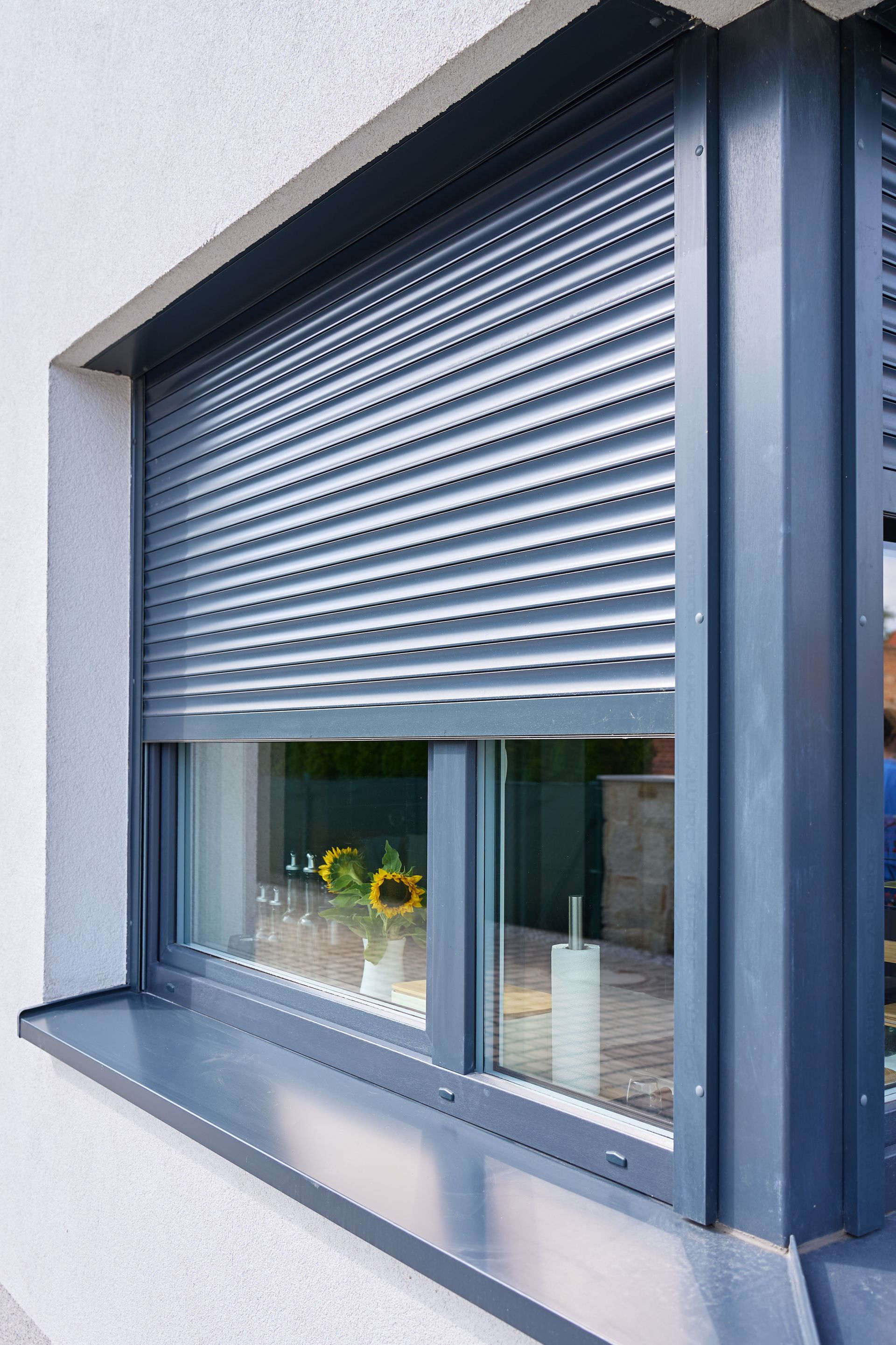 Volet roulant métallique gris partiellement fermé sur la façade d’un bâtiment