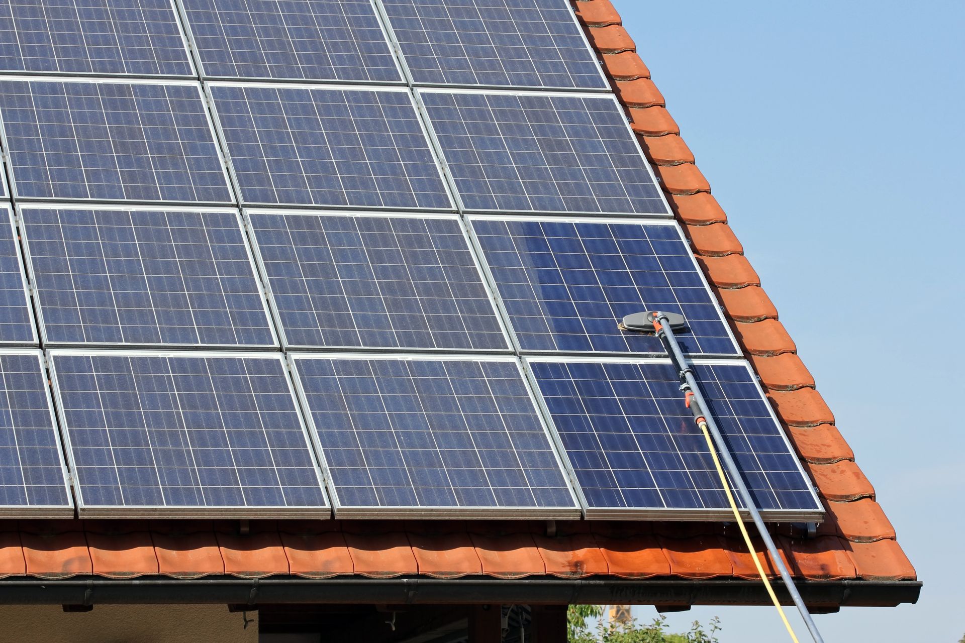 Panneaux solaires sur un toit en tuiles avec une perche de nettoyage.