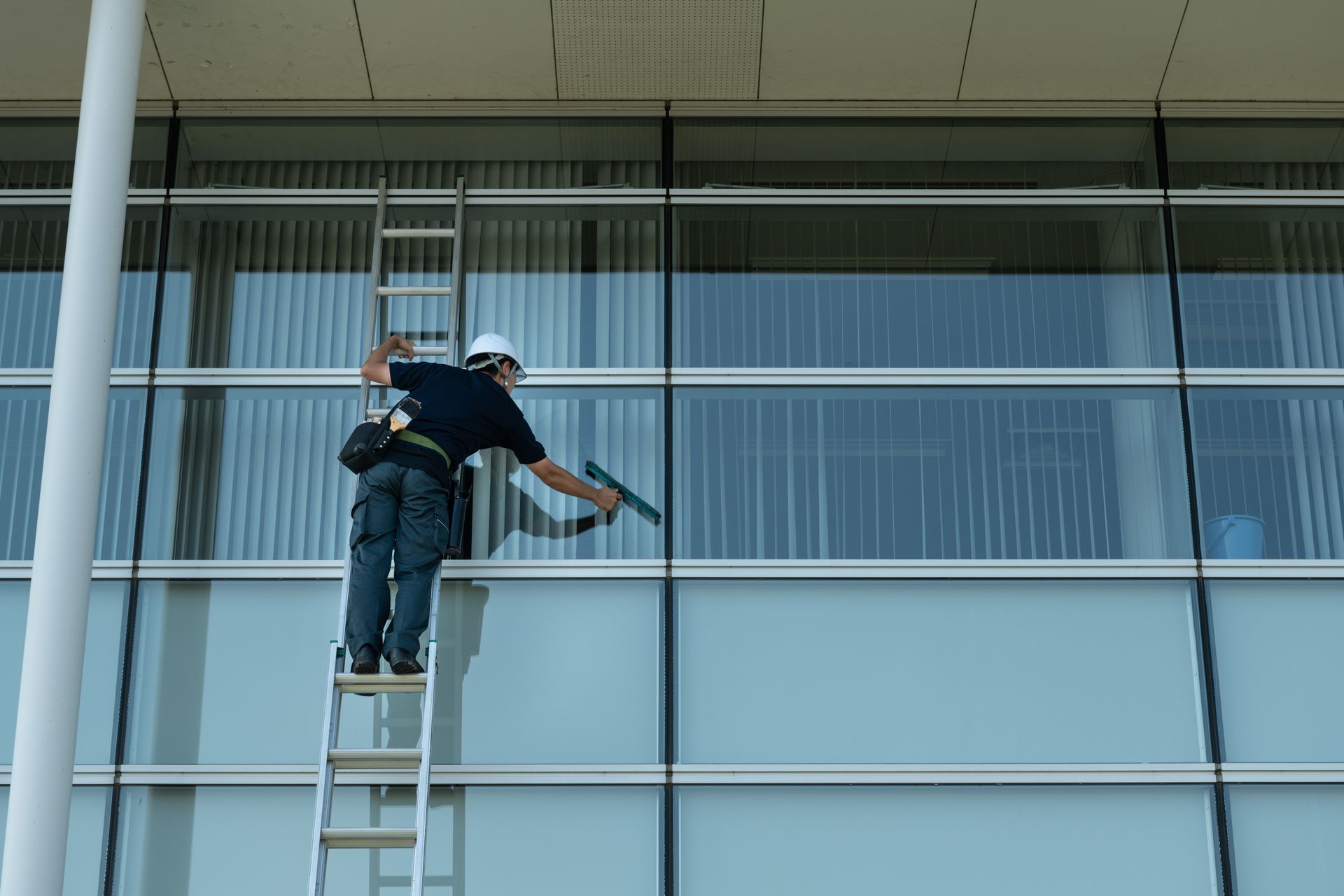 Un ouvrier sur une échelle nettoyant la façade vitrée d’un immeuble de bureaux