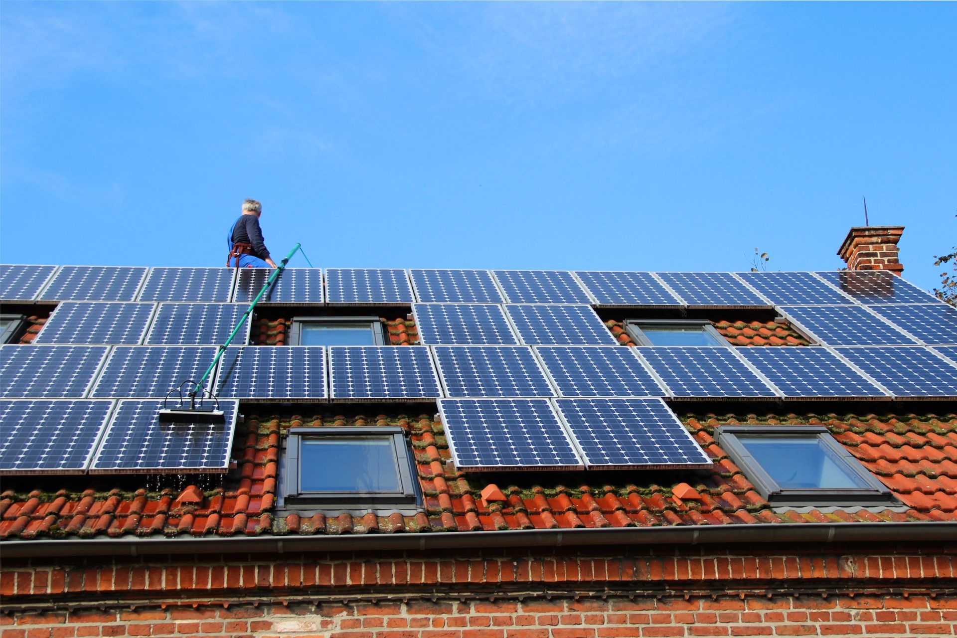 Un ouvrier nettoie des panneaux solaires installés sur un toit en tuiles