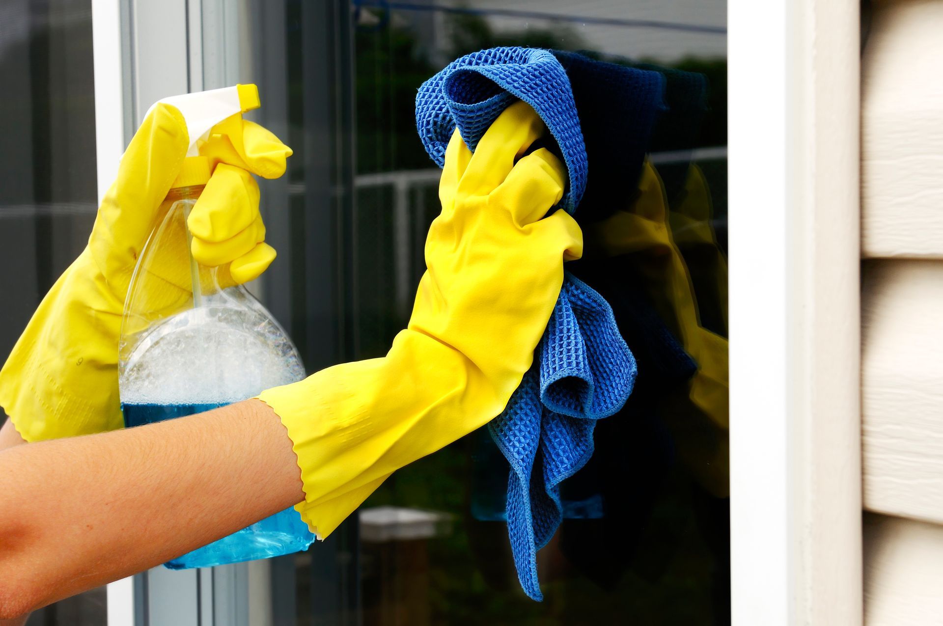 Des mains gantées de jaune nettoient une fenêtre avec un vaporisateur et un chiffon bleu