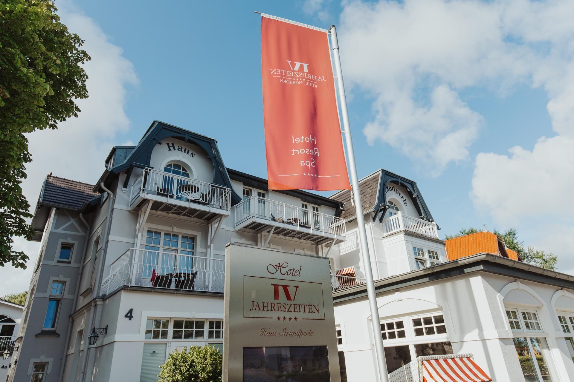 Elegantes weißes Gebäude mit Turm; rote Fahnen, Sitzbereich im Freien und Schilder an einem sonnigen Tag.