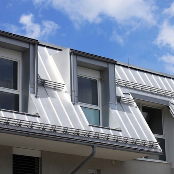 Ein weißes Gebäude mit Mansarddach und mehreren Dachgauben vor einem bewölkten Himmel.