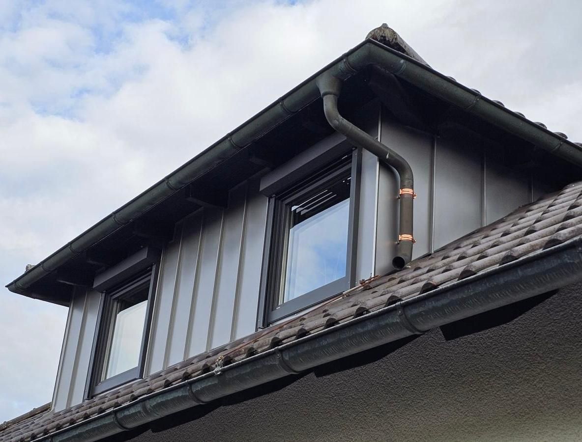 Ein weißes Gebäude mit Mansarddach und mehreren Dachgauben vor einem bewölkten Himmel.