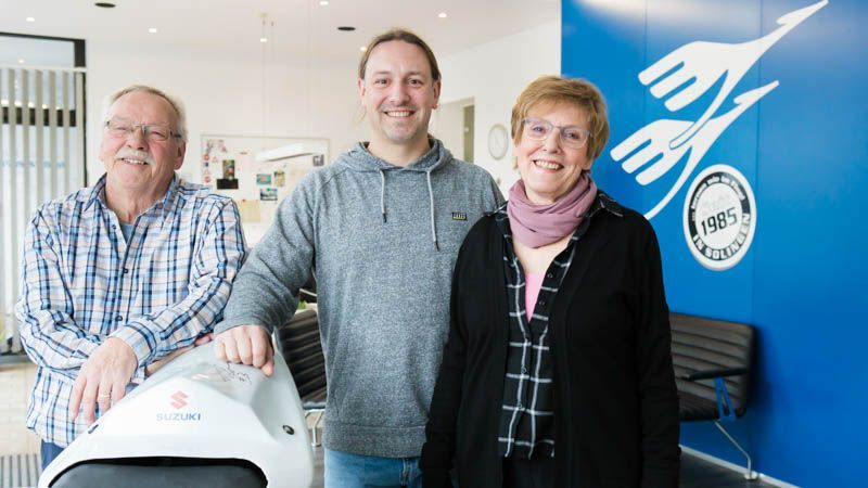 Drei Personen stehen vor einem Suzuki-Motorrad