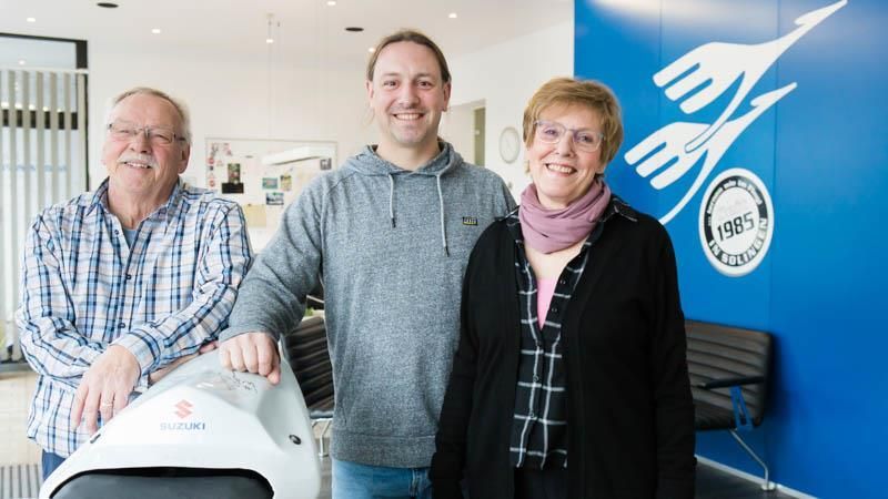 Drei Personen stehen vor einem Suzuki-Motorrad