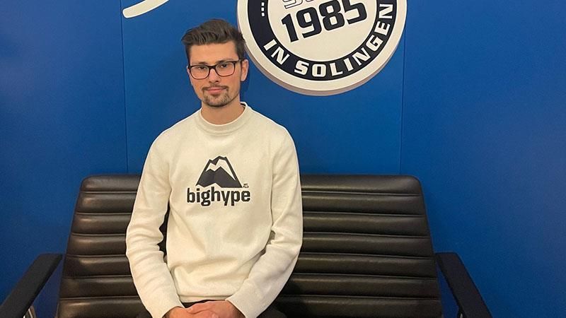 Ein Mann mit einem Bighype-Pullover sitzt auf einer Bank