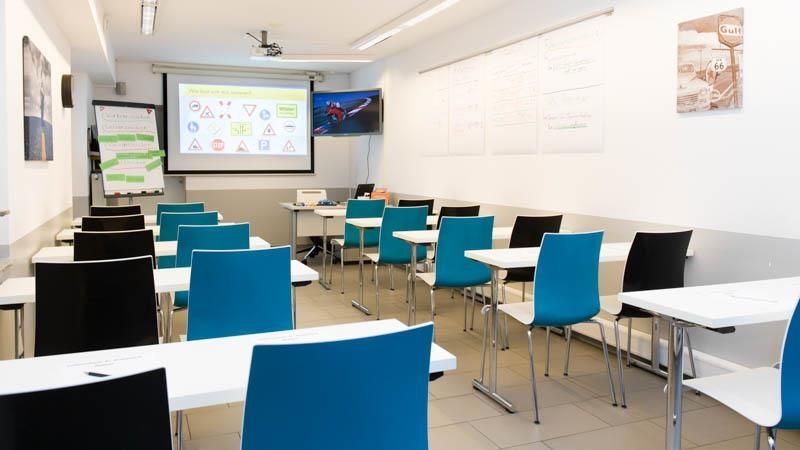 Ein leeres Klassenzimmer mit blauen Stühlen und weißen Tischen