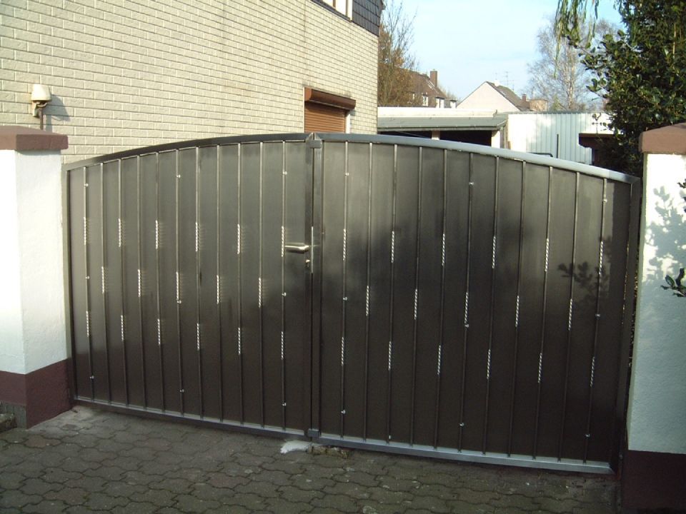 Ein schwarzes Tor steht zu einer Einfahrt vor einem Backsteingebäude offen