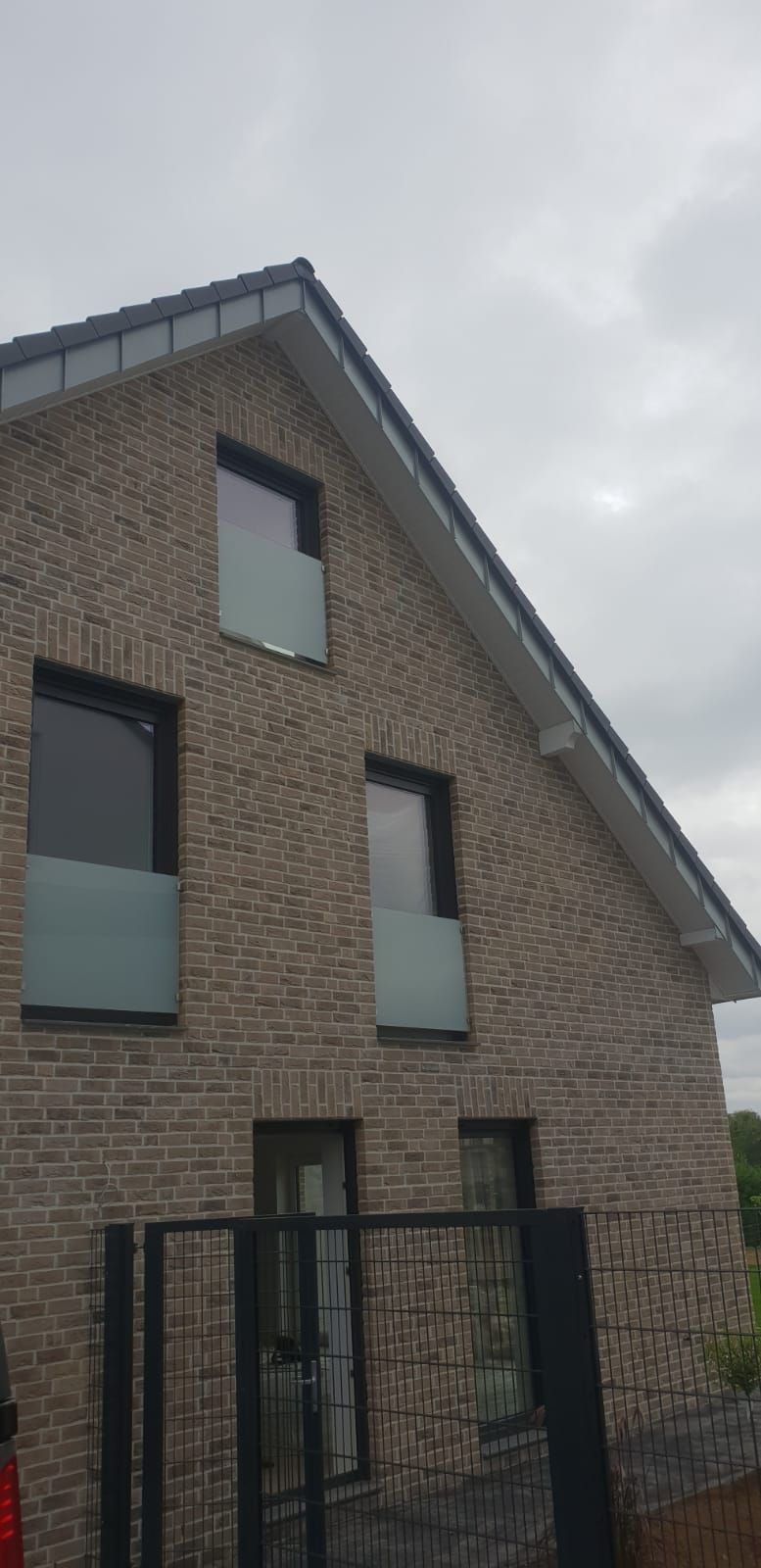 Ein Backsteinhaus mit Balkon und einem Zaun davor.