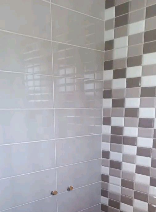 Mur de salle de bain carrelé de gris clair avec une frise verticale de carreaux à damier gris et marron