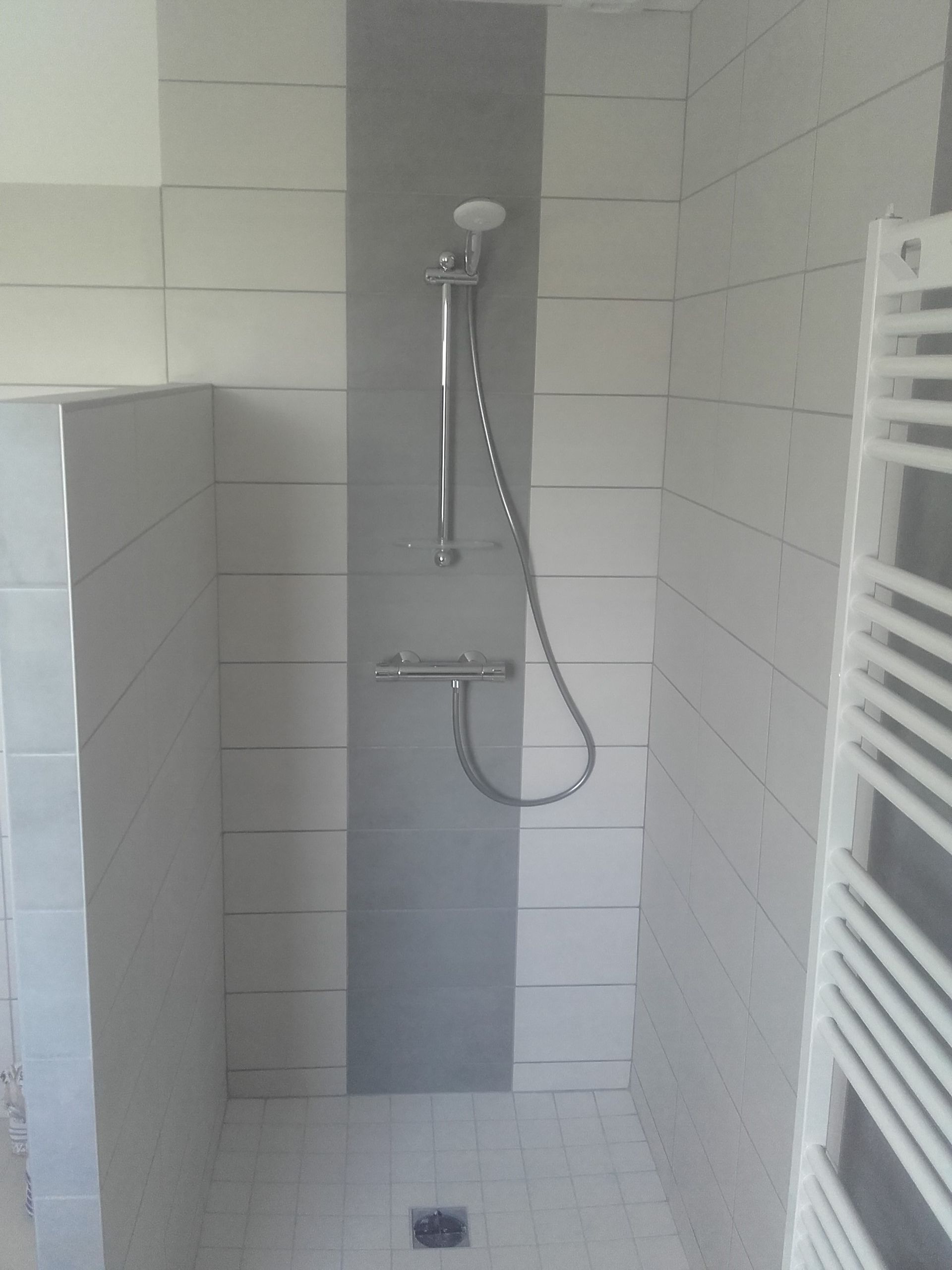 Petite cabine de douche carrelée avec pommeau de douche à main et sèche-serviettes blanc.