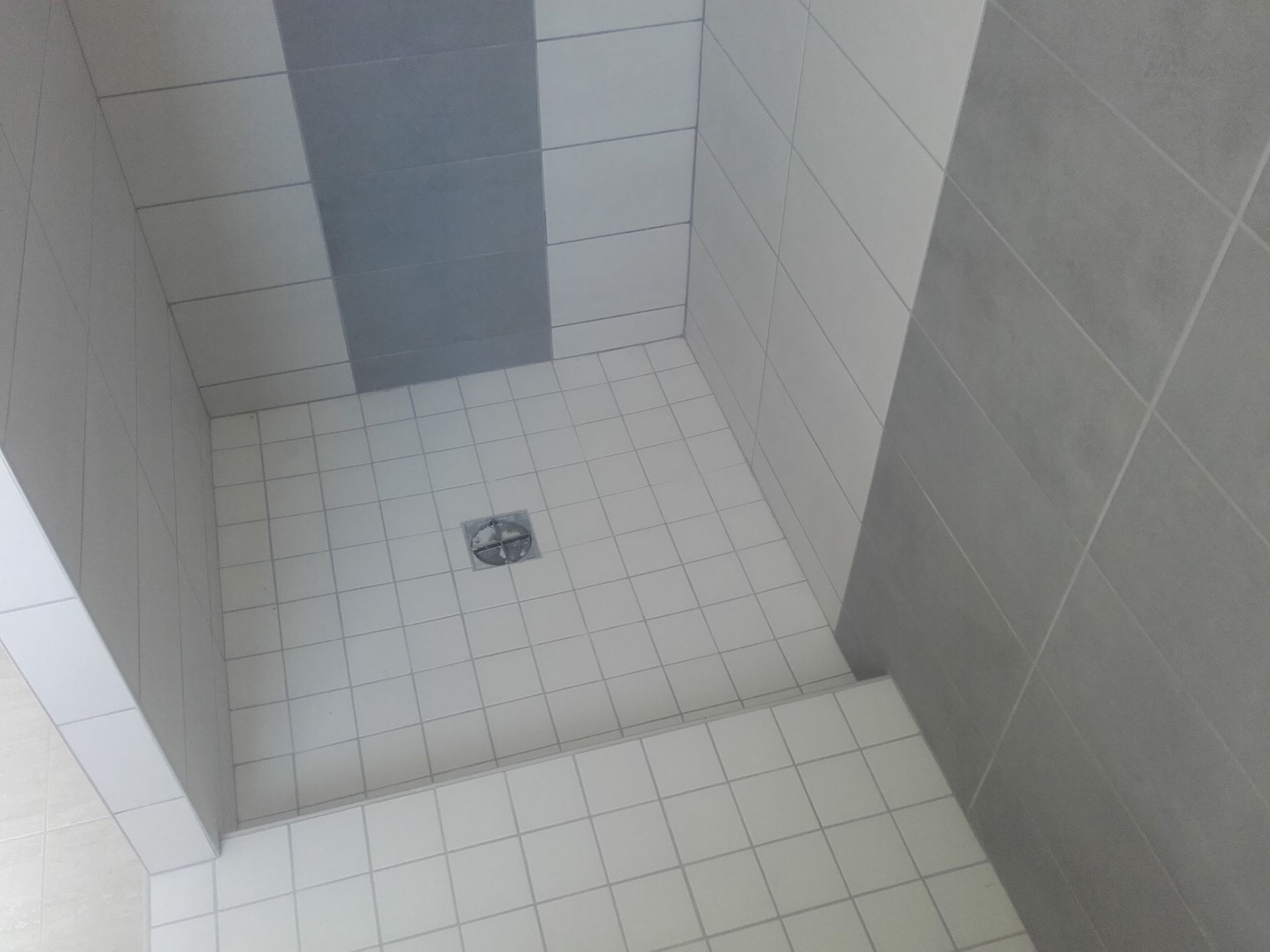 Cabine de douche carrelée avec bonde centrale et faïence grise décorative sur le mur du fond