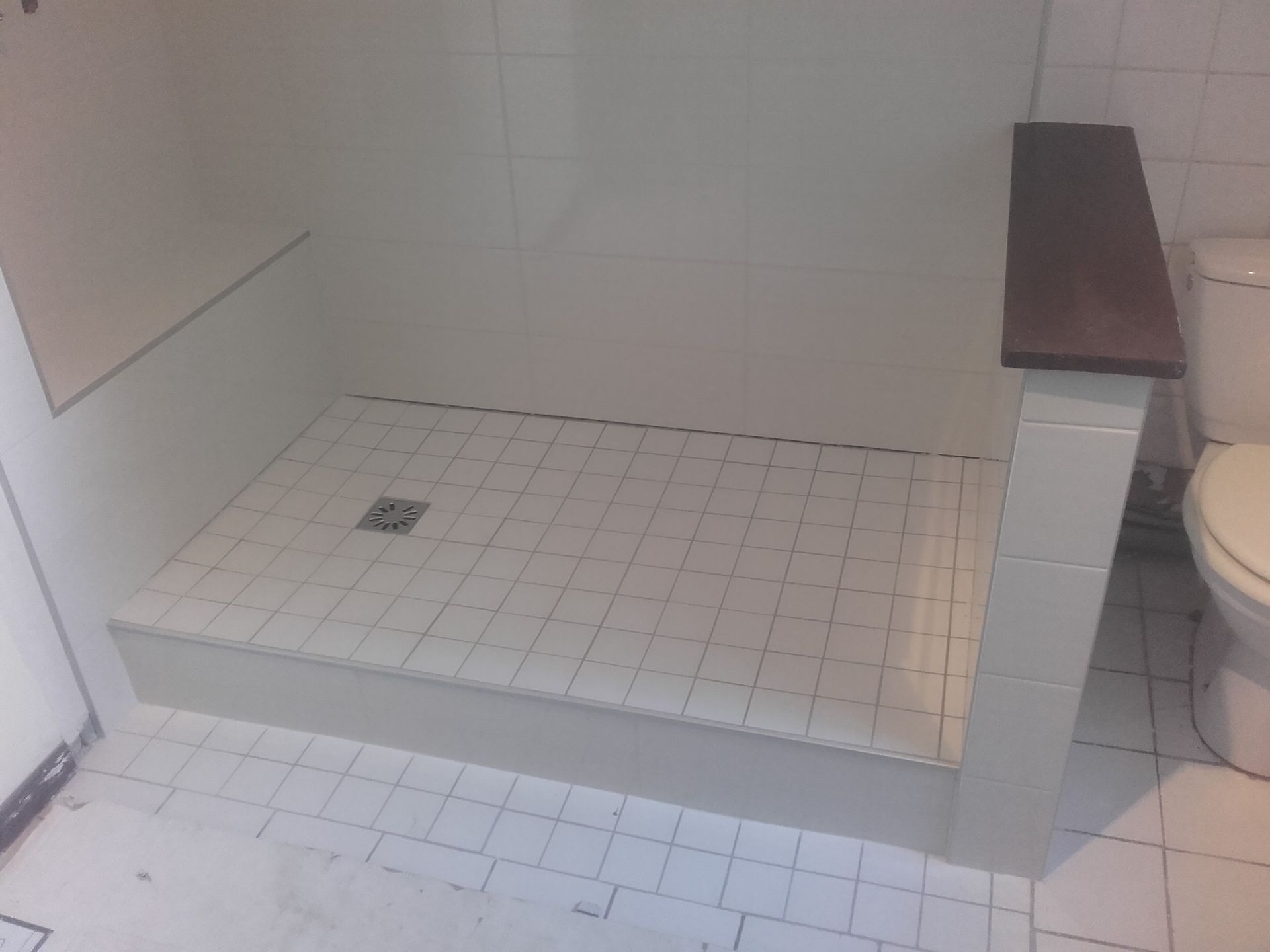 Douche à l'italienne carrelée avec murs blancs, petite bonde et banc en bois.