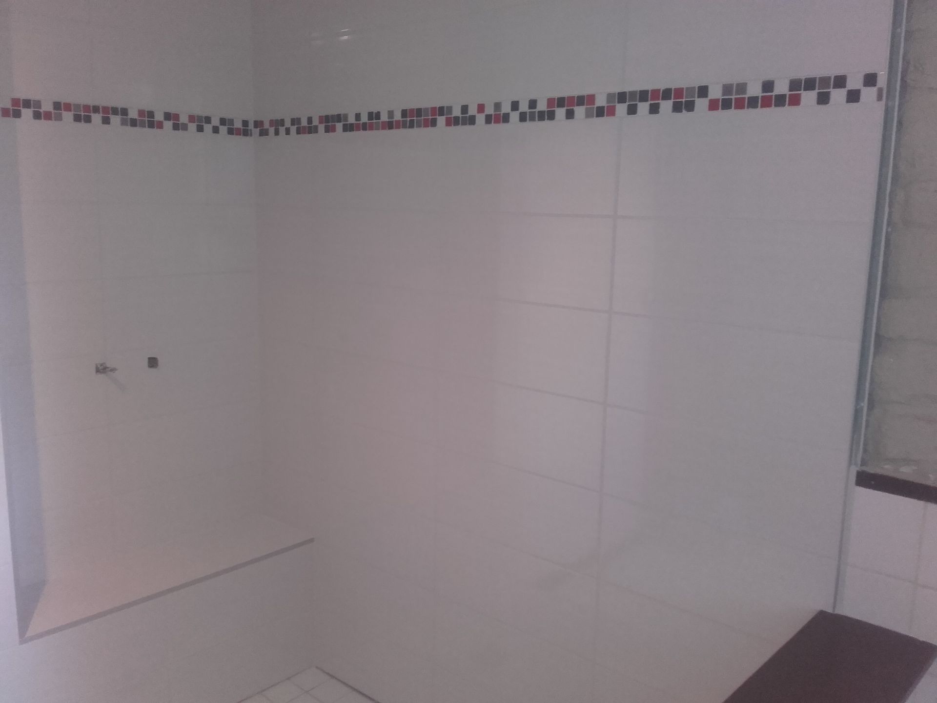 Coin de douche ou de salle de bains carrelé de blanc, vide, avec une frise décorative en haut.