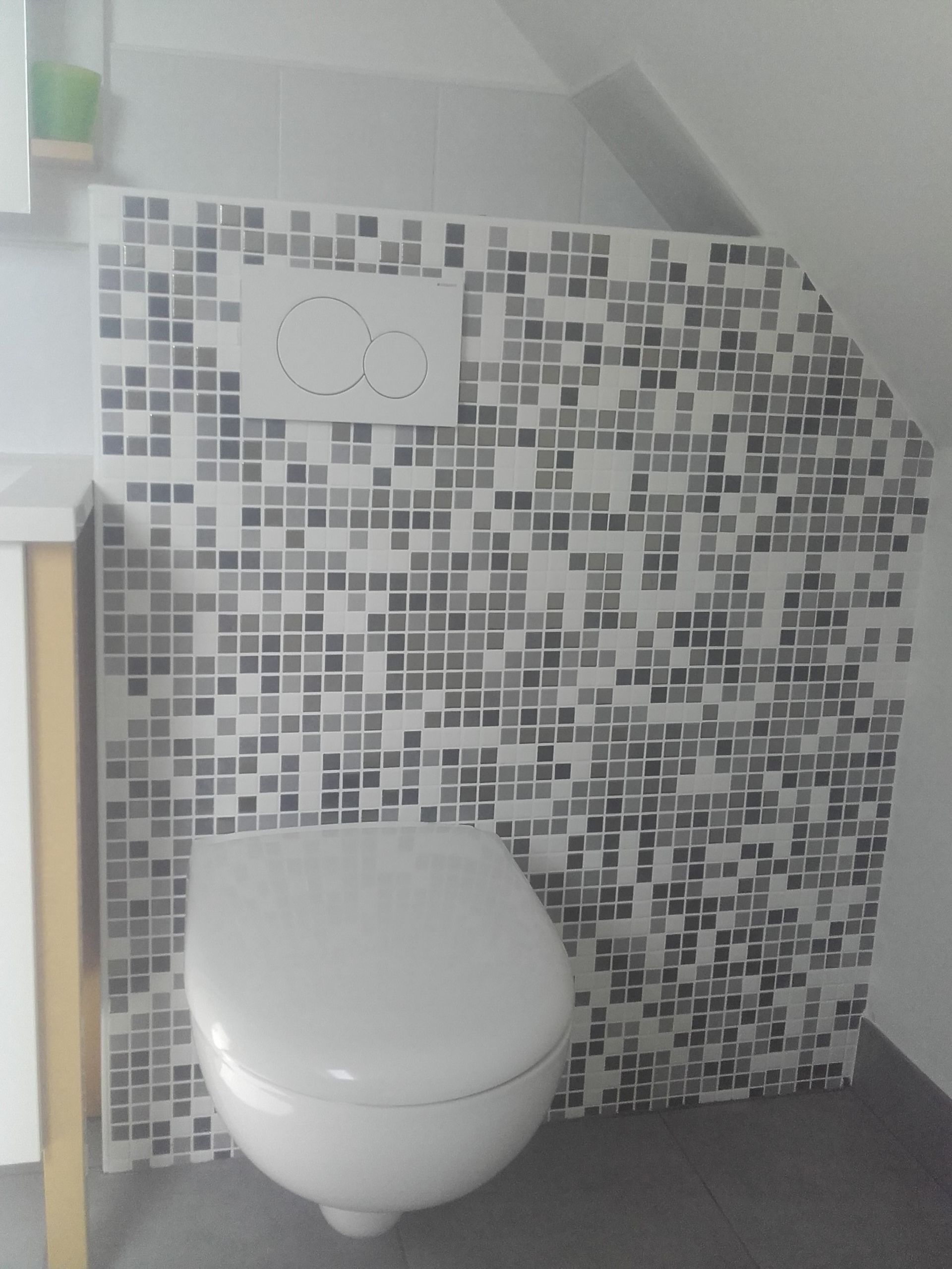 Petite salle de bains carrelée avec toilettes suspendues et mécanisme de chasse d'eau.