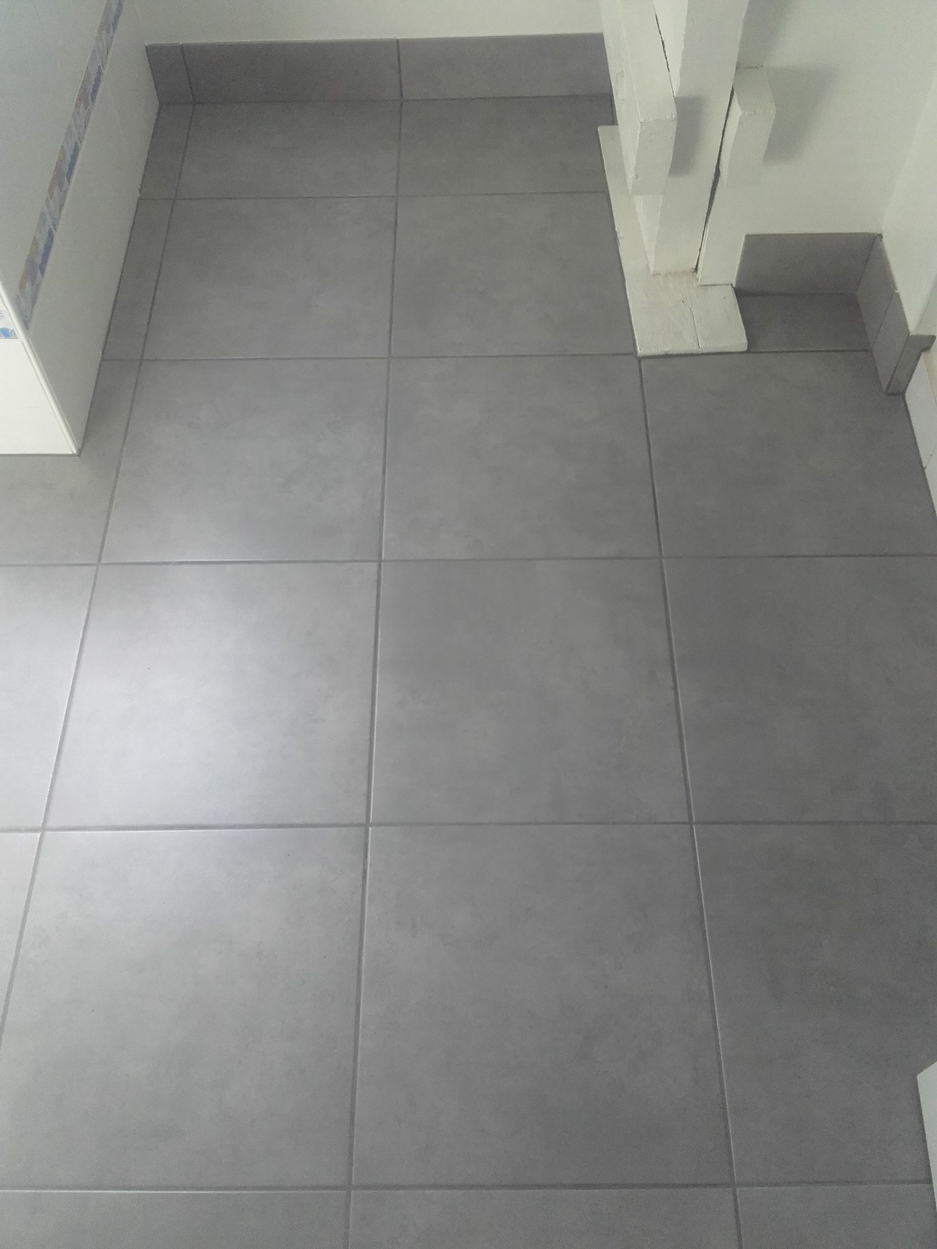 Sol carrelé gris vide dans un coin de toilettes ou de couloir.