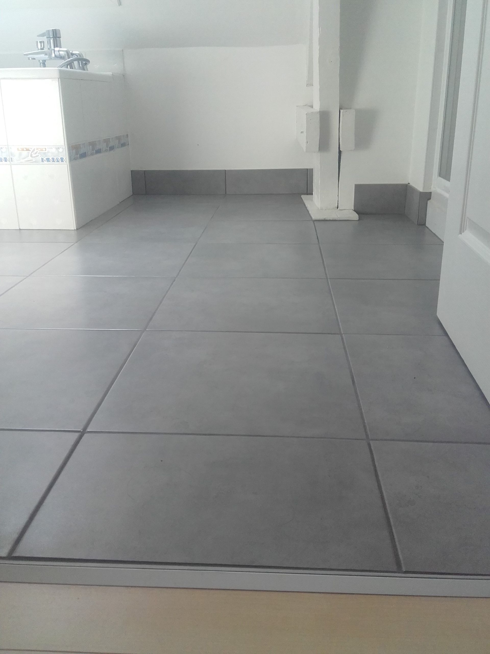 Pièce intérieure vide avec sol carrelé gris, murs blancs et un petit coin lavabo sur la gauche.