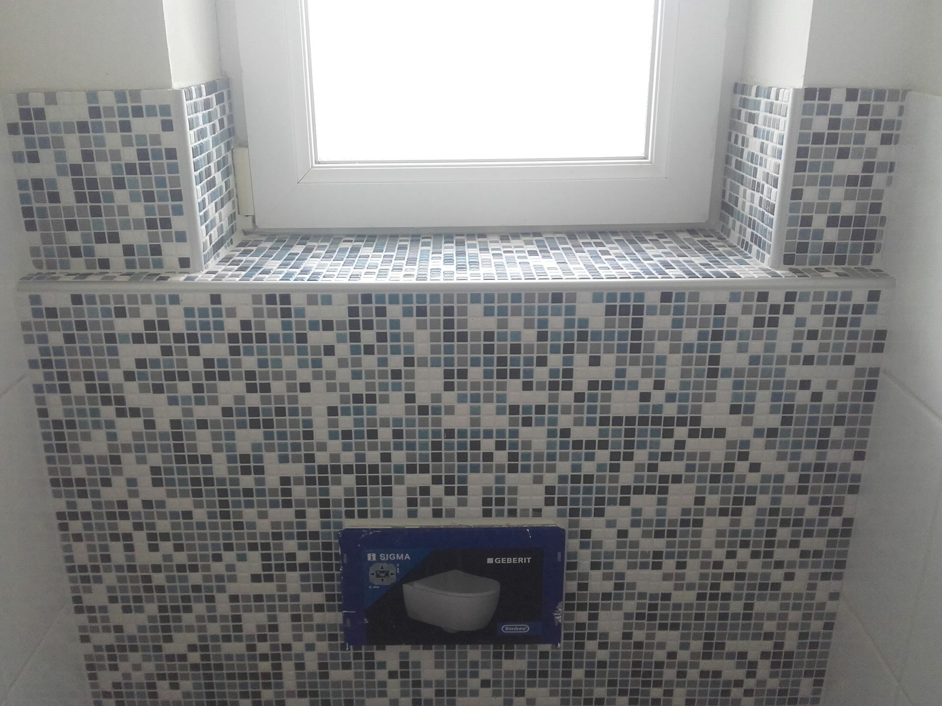 Mur carrelé de salle de bain avec une fenêtre au-dessus et un distributeur de savon encastré au centre
