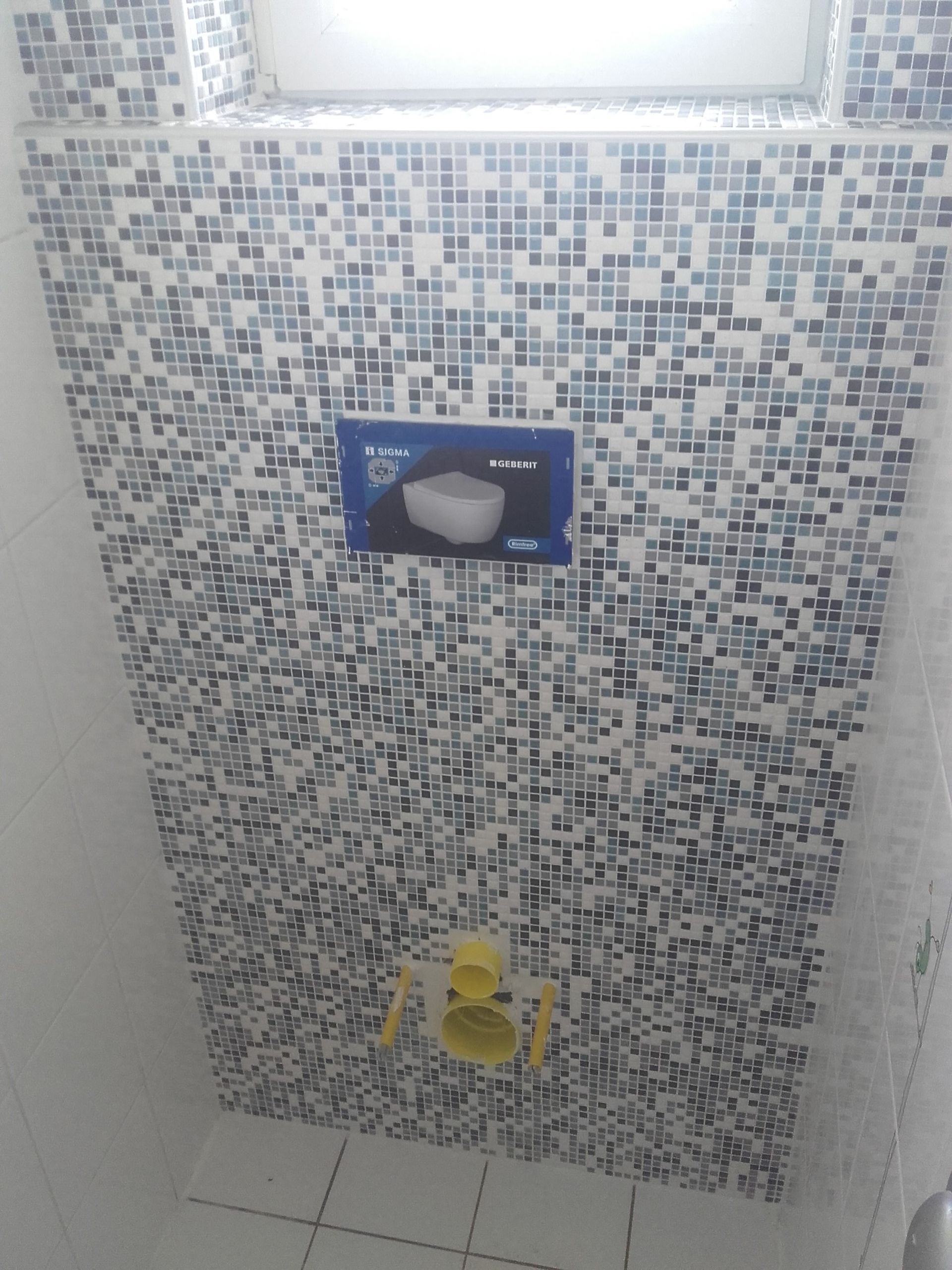 Mur de douche carrelé en mosaïque avec une étagère bleue et une figurine jaune près du sol.