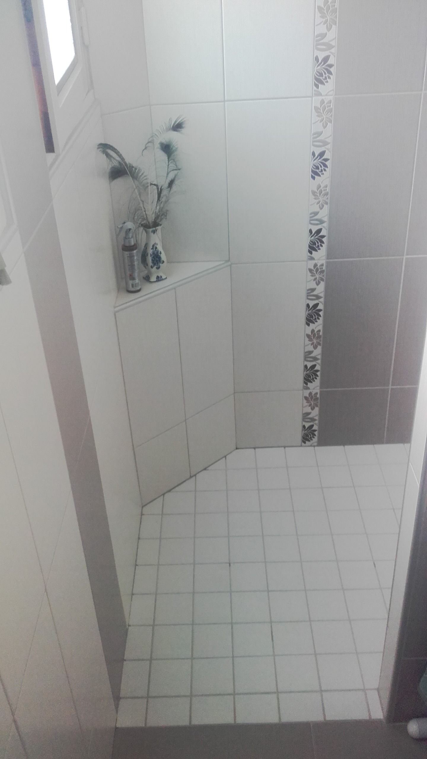 Petite cabine de douche carrelée blanche avec pommeau de douche mural et carreaux décoratifs.