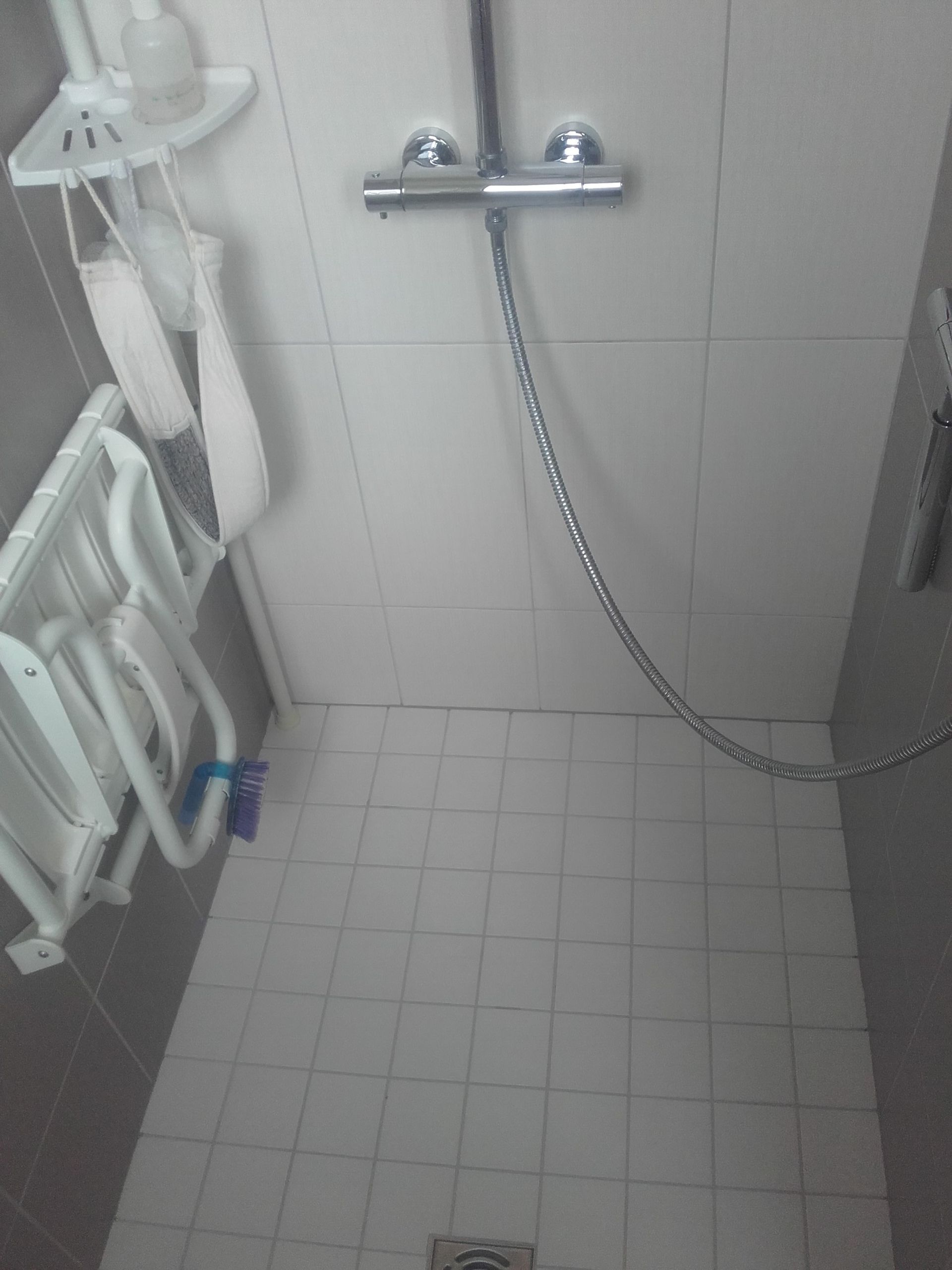 Petite salle de douche carrelée avec une douche murale et une chaîne suspendue au-dessus de la paroi.